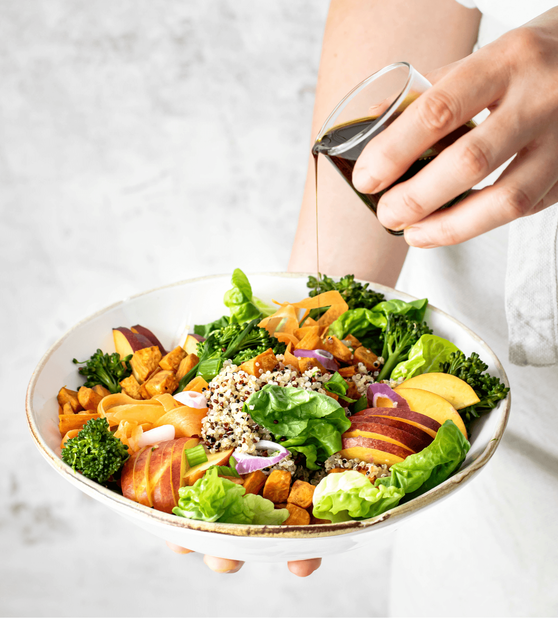 Uma mão colocando molho em um prato com salada verde variada.