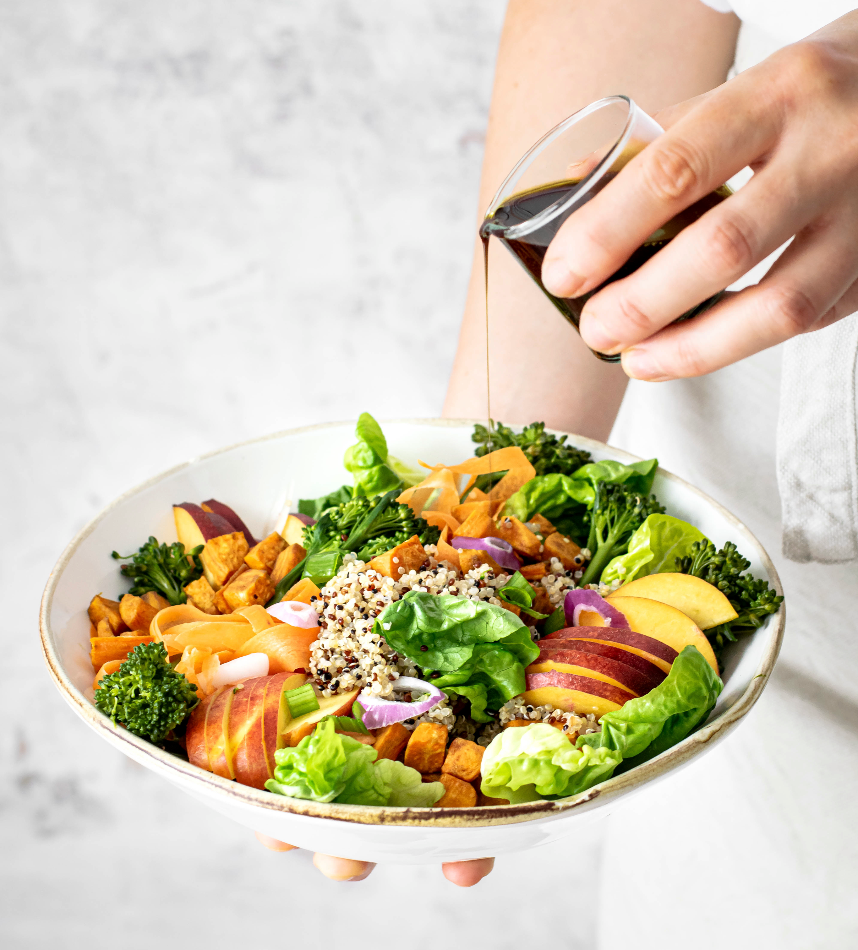 Uma mão colocando molho em um prato com salada verde variada.
